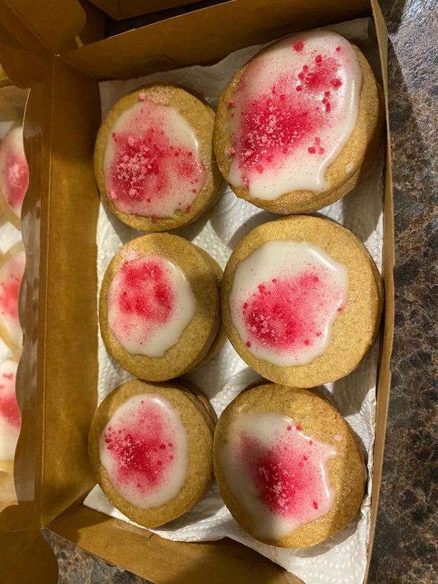 Six small iced bakes with pink sprinkles, packed in a kraft box.